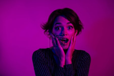 Photo portrait of attractive young woman touch face shocked dressed stylish overall clothes isolated on neon light pink color background.
