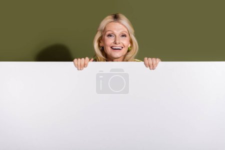 Foto des reifen Alters Frau Promoter hält Werbetafel leer leere Fläche für kostenlose öffentliche Werbung isoliert auf khakifarbenem Hintergrund.
