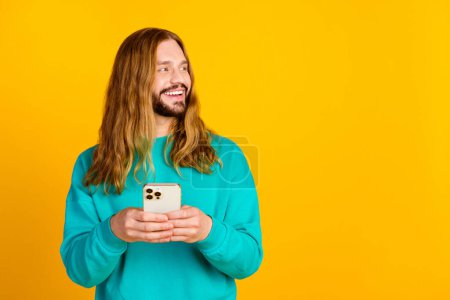 Portrait of attractive man hold smart phone look empty space advert isolated on yellow color background.