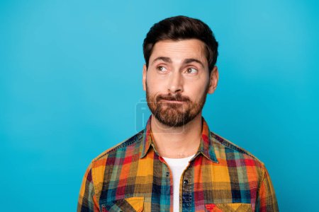 Portrait of intelligent guy with stubble wear checkered shirt thoughtfully look at offer empty space isolated on blue color background.