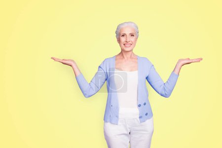 Beautiful nice cheerful smiling gray-haired old lady wearing casual, showing two options with palms. Isolated over pastel violet purple background.