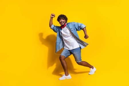 Full body photo of attractive young man dance walk good mood wear trendy denim clothes red scarf isolated on yellow color background.