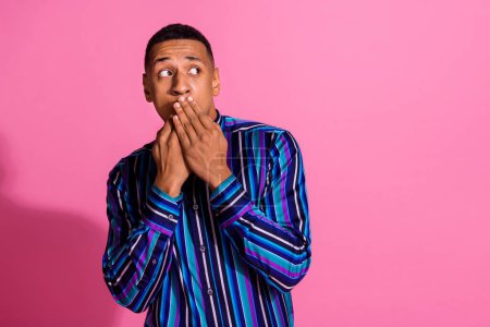 Photo of impressed scared guy wear striped shirt arms close mouth looking empty space isolated pink color background.