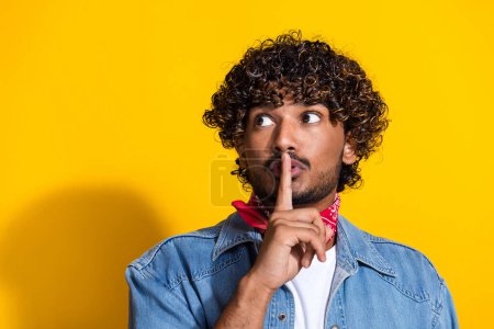 Photo portrait of attractive young man keep secret look empty space wear trendy denim clothes red scarf isolated on yellow color background.