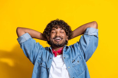 Photo portrait of attractive young man arms behind head enjoy sleep wear trendy denim clothes red scarf isolated on yellow color background.
