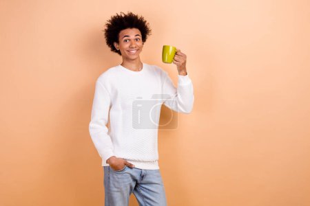 Foto von fröhlichen Mann tragen weiße trendige Kleidung halten Becher leckeres Koffein erfrischendes Getränk isoliert auf beige Hintergrund.