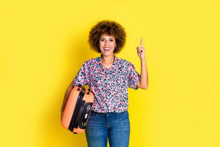 Foto von glänzenden aufgeregten Frau tragen Animal-Print-Shirt hält Gepäck zeigt mit dem Finger nach oben leeren Raum isoliert gelbe Farbe Hintergrund.