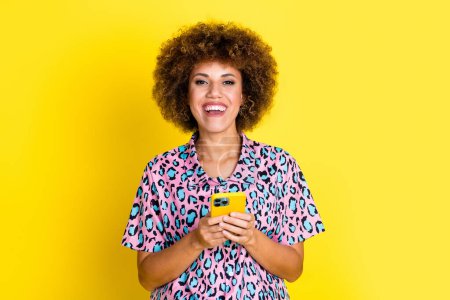 Photo of cheerful positive woman wear animal print shirt texting sms modern gadget empty space isolated yellow color background.
