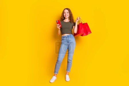 Foto de adorable linda chica vestida ropa elegante hacer la compra de entrega en línea pedido aislado en el fondo de color amarillo.