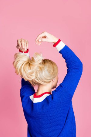 Vertikal hinten Foto der hübschen Dame Arme werfen perfekte wellige Haare tragen blauen Pullover isoliert auf rosa Hintergrund.
