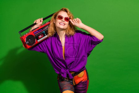 Photo portrait of pretty young girl hold boombox enjoy music look empty space wear trendy purple outfit isolated on green color background.