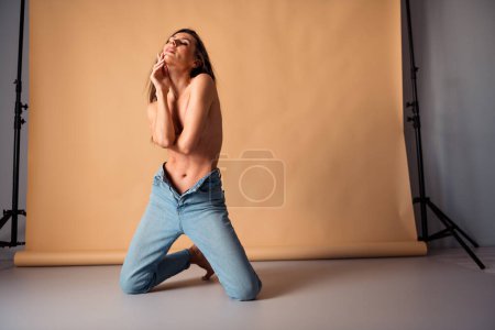 Photo non retouchée d'une femme étonnante assise toucher le visage sentir passion sur photo session isolé studio couleur pastel arrière-plan.