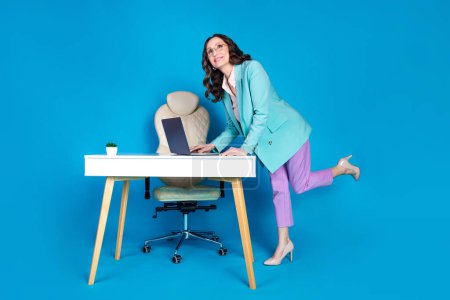 Full length photo of smiling dreamy lady dressed jacket sending emails modern gadget empty space isolated blue color background.