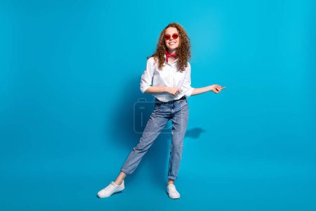 Foto retrato de la joven dama bailando discoteca gafas de sol verano ropa de moda ropa blanca aislada en el fondo de color azul.
