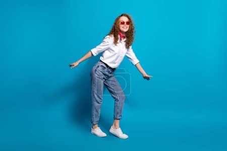 Foto retrato de la joven agradable gafas de sol vacaciones de verano danza disco desgaste ropa blanca de moda aislado sobre fondo de color azul.