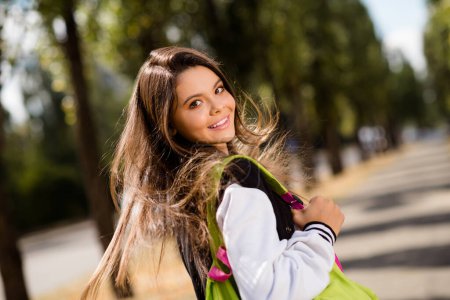 Photo de l'adorable étudiant avec flottement sur les cheveux du vent habillé veste élégante tenir sac à dos profiter de la marche par temps ensoleillé à l'extérieur.
