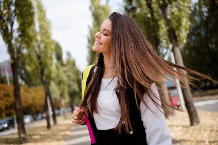 Photo d'un étudiant de bonne humeur aux cheveux raides veste élégante sac à dos sur l'épaule amour de marcher après les cours dans le parc à l'extérieur.
