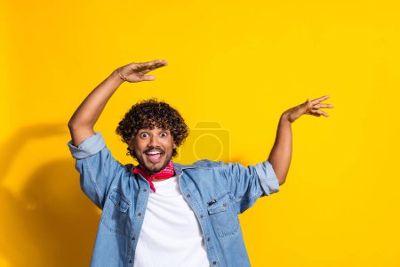 Photo portrait of nice young male raise hands excited dancing dressed stylish denim outfit red scarf isolated on yellow color background.