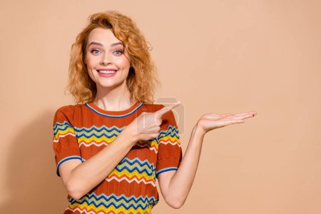 Foto von zahm strahlende Frau gekleidet Ornament T-Shirt richtet sich an Produkt auf Arm leeren Raum isoliert auf pastellfarbenem Hintergrund.