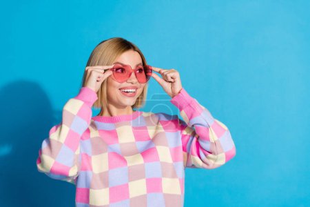 Photo portrait of pretty young girl touch sunglass celebrate look empty space wear trendy pink outfit isolated on blue color background.