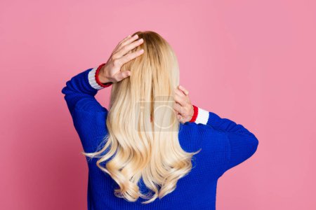 Hinten Foto der hübschen Dame Arme berühren glänzende Haare tragen blauen Pullover isoliert auf rosa Hintergrund.