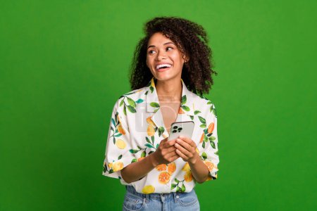 Photo of cheerful dreamy woman dressed print shirt texting modern gadget looking empty space isolated green color background.