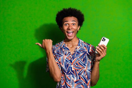 Photo of shocked funky man dressed print shirt chatting modern gadget thumb empty space isolated green color background.