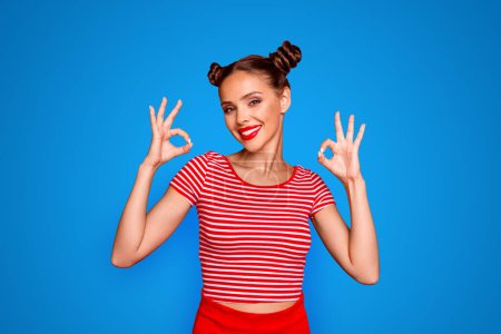 Close up portrait of happy, pretty, confident and smiling girl striped shirt showing ok sign standing on red background.