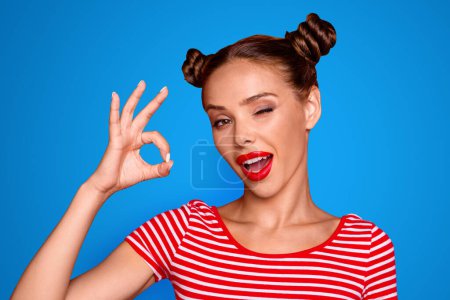 Close up portrait of happy girl with wide open mouth and wink eye gesturing ok sign isolated on vivid red background.