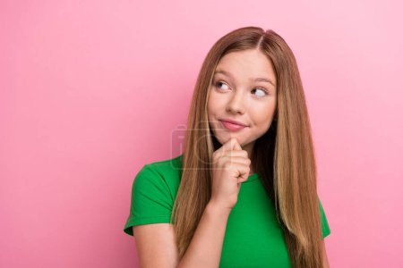 Photo portrait of pretty teenager girl touch chin minded empty space dressed stylish green outfit isolated on pink color background.