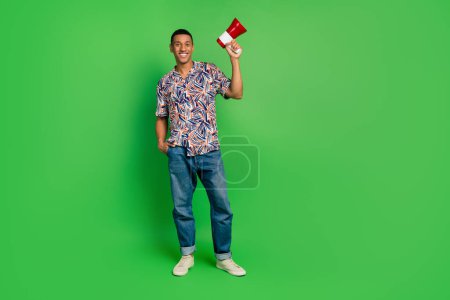Full body portrait of cheerful nice man hold loudspeaker empty space ad isolated on green color background.