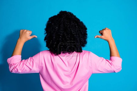 Rear portrait of pretty young woman point fingers hairdo wear pink shirt isolated on blue color background.
