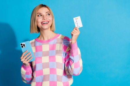 Photo portrait of pretty young girl hold gadget credit card look empty space wear trendy pink outfit isolated on blue color background.