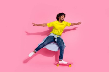 Photo of amazed cheerful glad man wear trendy yellow clothes riding skateboard empty space isolated on pink color background.