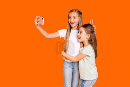 Portrait de deux belles jolies joyeux joyeux filles gaies positives montrant v-signe comme oreilles de lièvre tromper faire selfie isolé sur fond jaune brillant vif
.