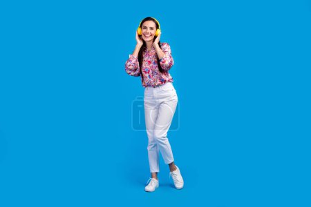 Full length photo of cute excited lady dressed print blouse enjoying songs earphones isolated blue color background.