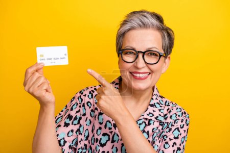 Photo portrait of pretty retired female hold point credit card wear trendy leopard print outfit isolated on yellow color background.