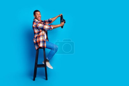 Pleine taille profil photo de beau jeune homme tenir roue vide espace usure chemise isolée sur fond de couleur bleue.