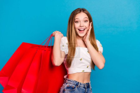 Foto de positiva chica feliz mantenga bolsas de compras impresionado fondo de color azul aislado.