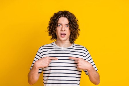 Portrait of young shocked teenager guy pointing fingers himself questioned and someone make him guilty isolated on yellow color background.