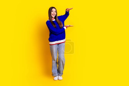 Foto de longitud completa de niña bastante adolescente mantenga medida espacio vacío desgaste ropa de punto de moda traje azul aislado en el fondo de color amarillo.