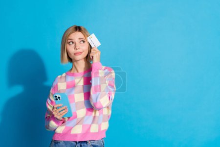 Photo portrait of pretty young girl hold gadget credit card look empty space wear trendy pink outfit isolated on blue color background.