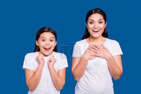 Close up photo pretty two people brown haired mum little daughter eyes mouth opened unbelievable arms point herself win lottery prize wearing white t-shirts isolated bright blue background.