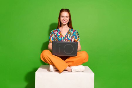 Ganzkörper-Porträt von hübschen jungen Mädchen sitzen Podium verwenden Netbook tragen Top isoliert auf hellgrünem Hintergrund.