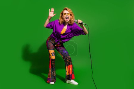 Photo portrait of pretty young girl hold microphone sing karaoke wear trendy purple outfit isolated on green color background.