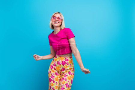 Foto retrato de encantadora joven toque gafas de sol baile de verano vestido elegante ropa rosa aislado sobre fondo de color azul.