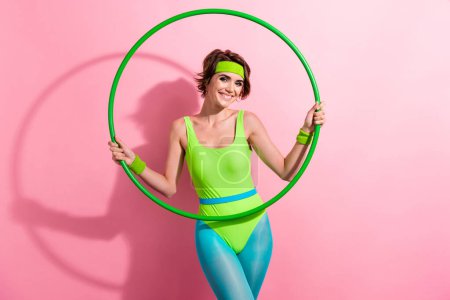 Fotoporträt der schönen jungen Dame halten hoolahoop Mode-Modell gekleidet stilvolle grüne Sport-Jumpsuit isoliert auf rosa Hintergrund.