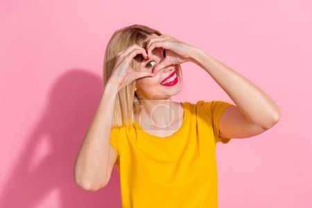 Foto von entzückenden hübschen Dame gekleidet gelbes T-Shirt zeigt Arme Herzbedeckung Auge isoliert rosa Farbe Hintergrund.