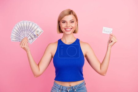 Porträt von netten jungen Mädchen halten Geldscheine Debitkarte tragen blaues Top isoliert auf rosa Hintergrund.