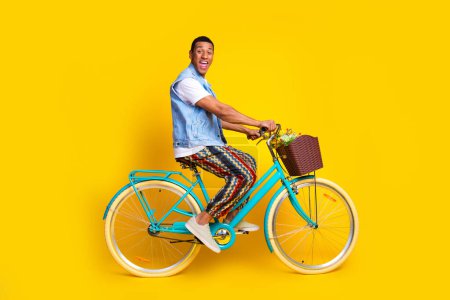 Full size photo of ecstatic man dressed denim vest over t-shirt riding cycle astonished staring isolated on yellow color background.